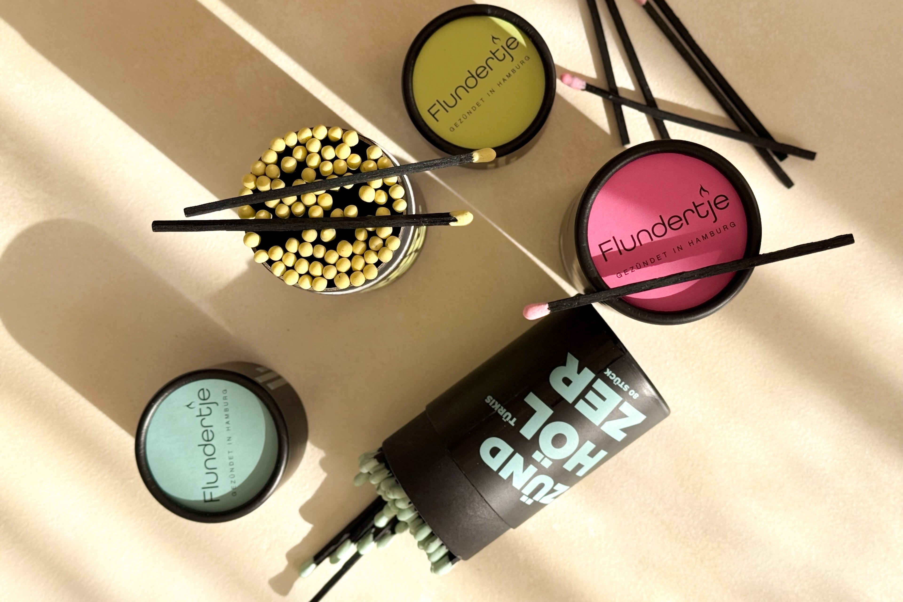 Streichhölzer in schwarzen Pappdosen in verschiedenen Farben als Flatlay